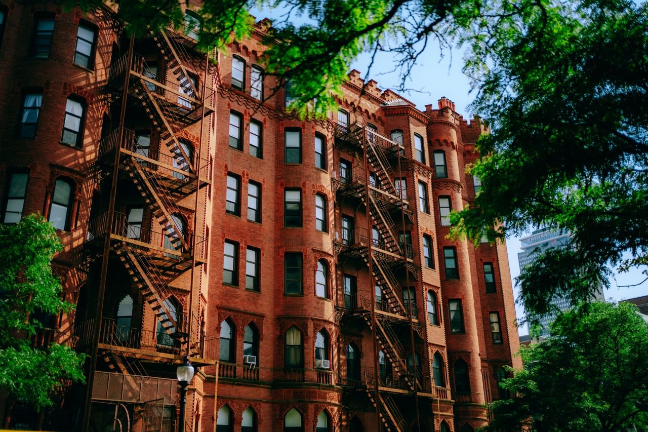 Traditional red brick building with metal fire escapes in an urban setting.